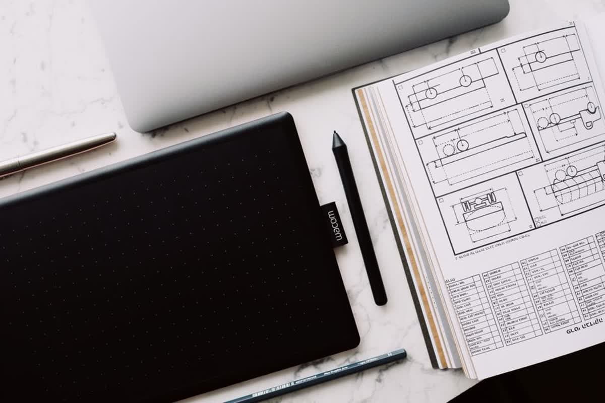 A graphic tablet, pen and open sketchbook arranged on a marble desk