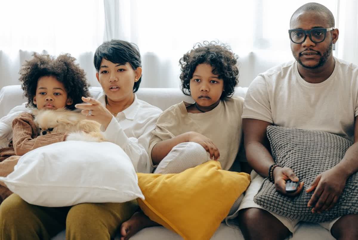 A family watching a screen together on a sofa at home with their dog